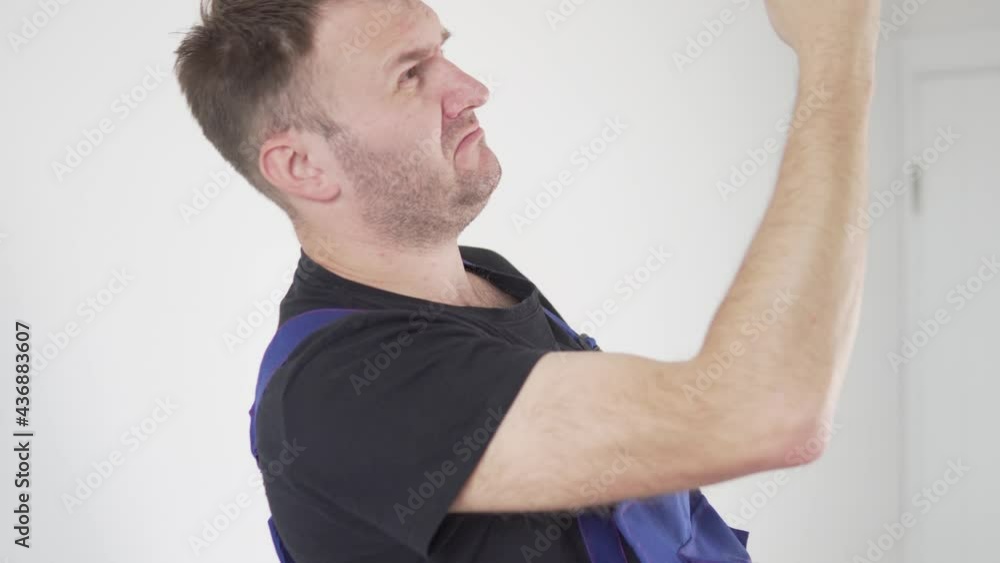 A male electrician in uniform twists a light bulb into a chandelier on the ceiling. A male electrician in uniform twists a light bulb into a chandelier on the ceiling.