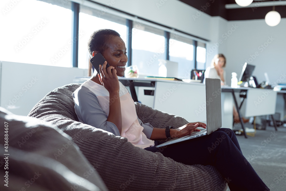 © Wavebreak Media - Smiling african american businesswoman sitting in armchair, talking by smartphone at work © Wavebreak Media - Smiling african american businesswoman sitting in armchair, talking by smartphone at work