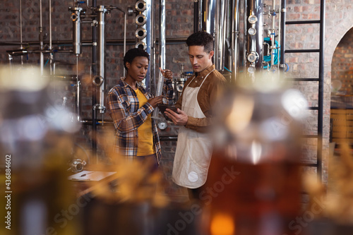 Diverse male and female worker discussing over digital tablet at gin distillery photo