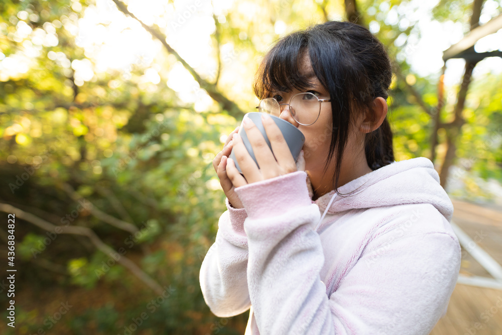 Asian girl in pink hoodie drinking tea standing in garden Asian girl in pink hoodie drinking tea standing in garden