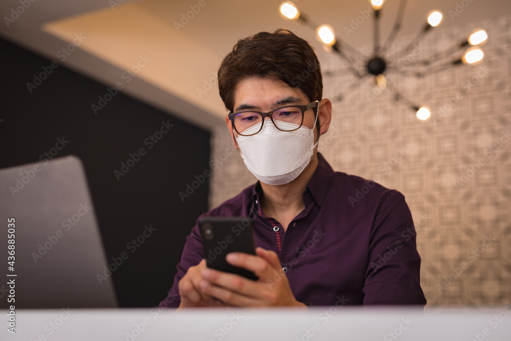 Asian businessman wearing face mask using smartphone and laptop in hotel lobby Asian businessman wearing face mask using smartphone and laptop in hotel lobby