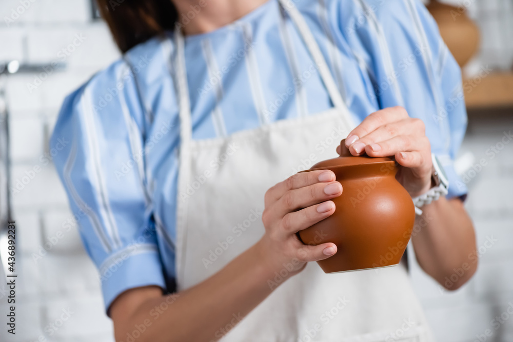 partial view of young adult woman holding clay pot in hands in kitchen partial view of young adult woman holding clay pot in hands in kitchen