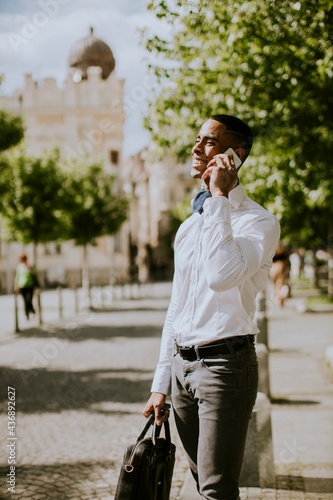 Young African American businessman using a mobile phone while waitng for a taxi on a street photo