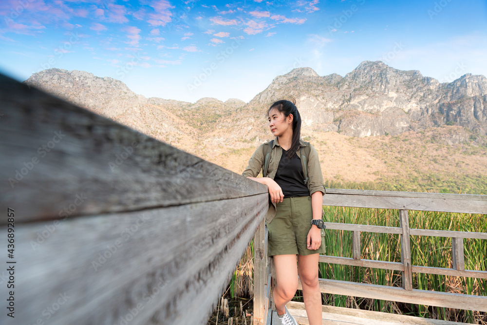 Naklejka premium Asian hikers carry heavy backpacking on a small Pavilion outdoor hiking path on a wooden bridge in a swamp with meadows with a blue mountain background. Khao Sam Roi Yot National Park