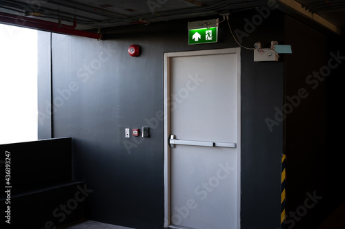 A fire exit with the sign and red alarm bell above the white door on the parking building.