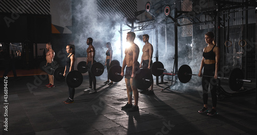 Group of athelte people exercising with heavy weights. Young men and fitness woman doing bodyweight exercises using barbell. Copy space. Sport concept