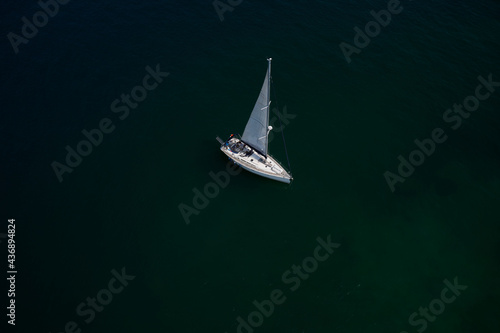 Boat with sails, blue water with high altitude. Large white boat with sails on blue water aerial view. Lonely sailboat on the water top view. Sailboat on Lake Garda, Italy.