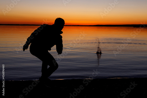 Silhouette of a man throws stones into the lake at sunset