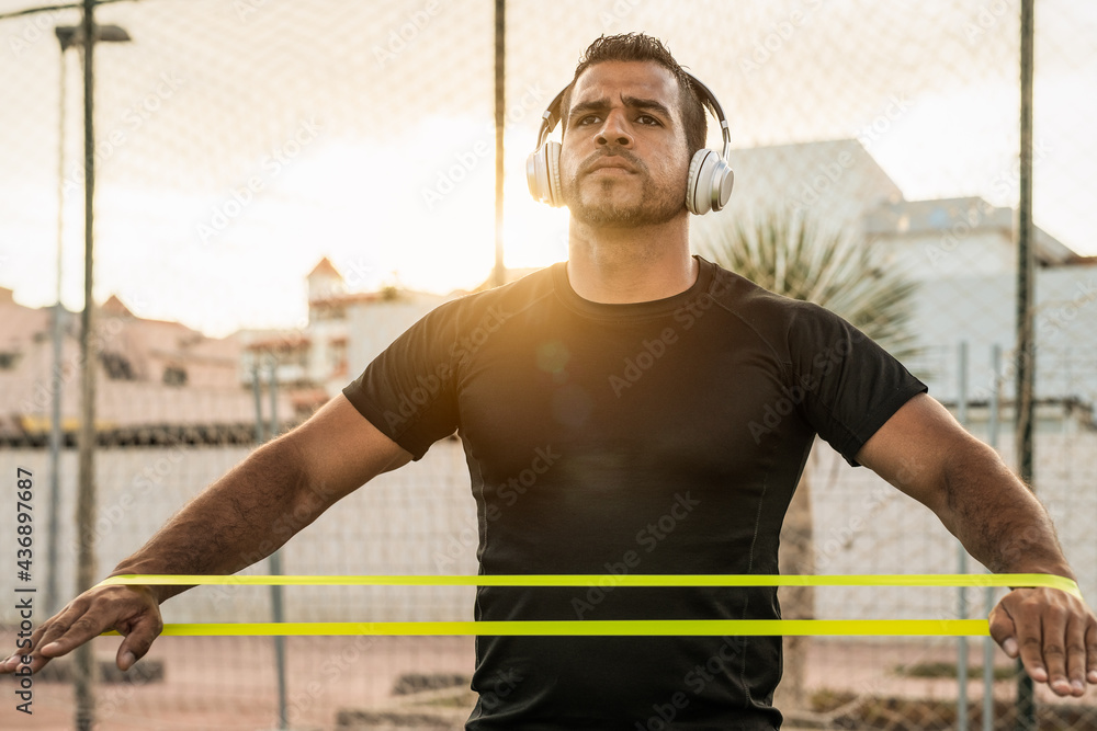 Man doing workout exercises session at sunset time - Young Hispanic male training hard while listening music with headphones