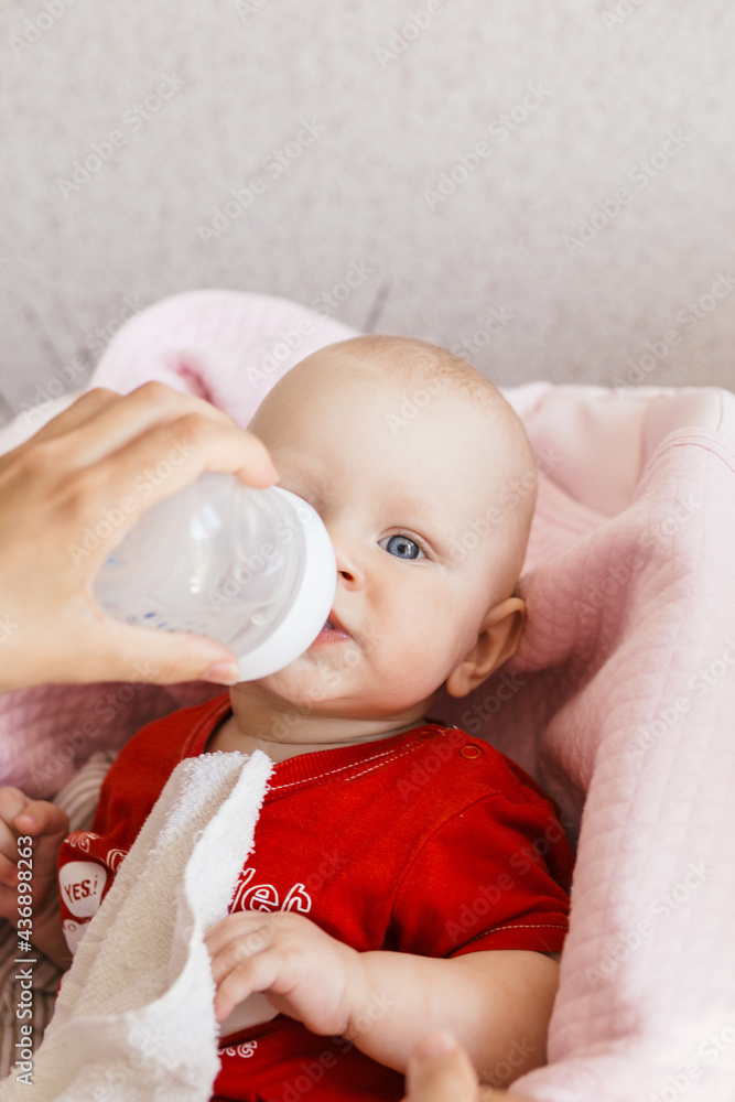 breastfed blonde baby in a red t-shirt tries first complementary foods from a small red spoon on a pink background breastfed blonde baby in a red t-shirt tries first complementary foods from a small red spoon on a pink background