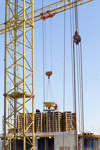 Hydraulic luffing jib tower cranes and workers being poured concrete into foundation. Cement pouring into formwork of building at construction site. Tower cranes constructing a new residential build