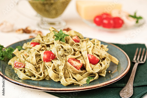 Fettuccine pasta with sauce pesto, cherry tomatoes, pine nuts and parmesan cheese on concrete background. Selective focus.