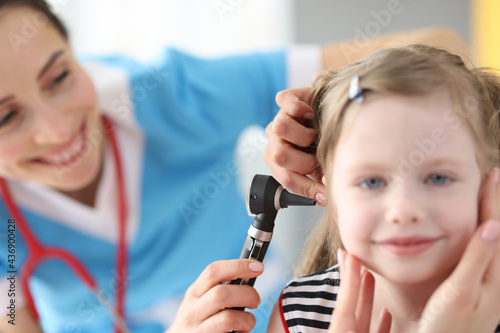 Female doctor conducts medical examination of ear with an otoscope to little girl