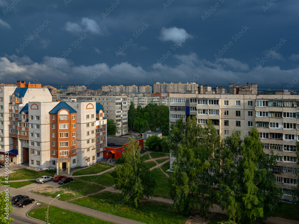 Sunrise at the residential area of the Cheboksary city with dark blue storm sky and clouds, sun rays and buildings.