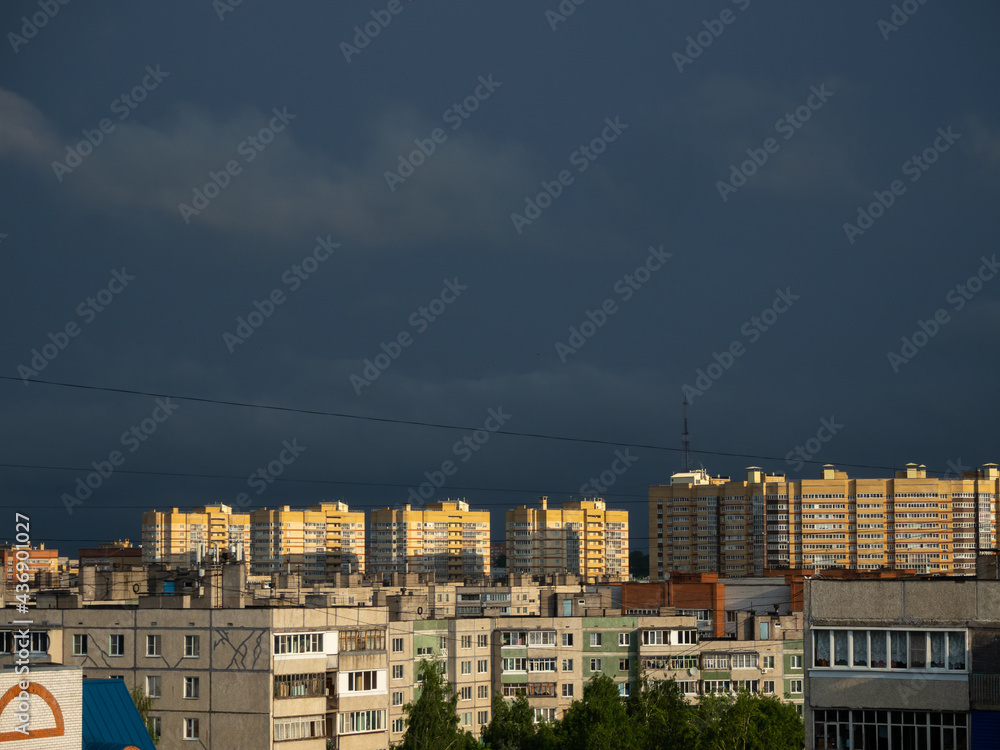 The sun shines on high-rise buildings at dawn. Sunrise at the residential area of the Cheboksary city with dark blue storm sky and clouds, sun rays and buildings.