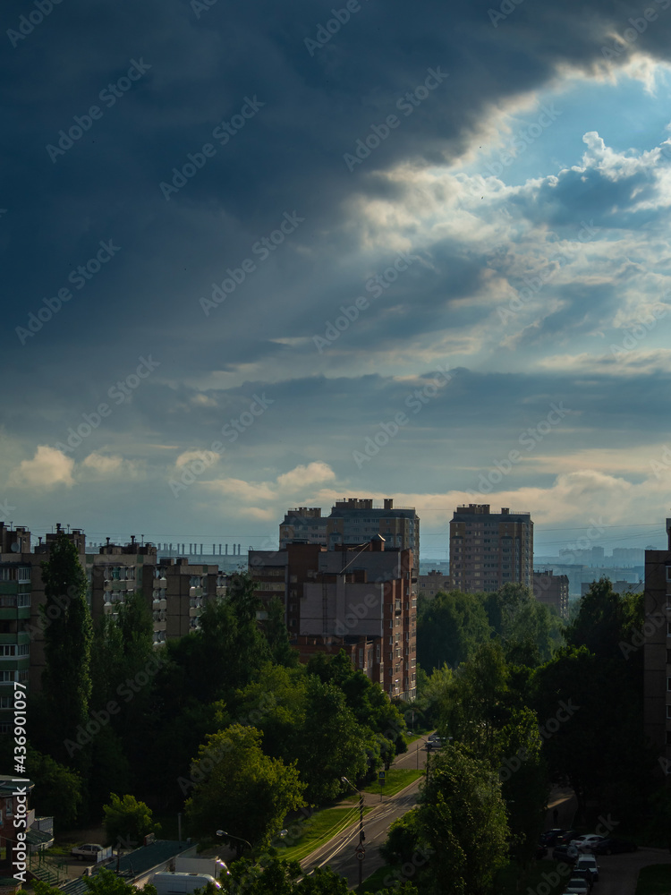 Sunrise at the residential area of the Cheboksary city with dark blue storm sky and clouds, sun rays and buildings.