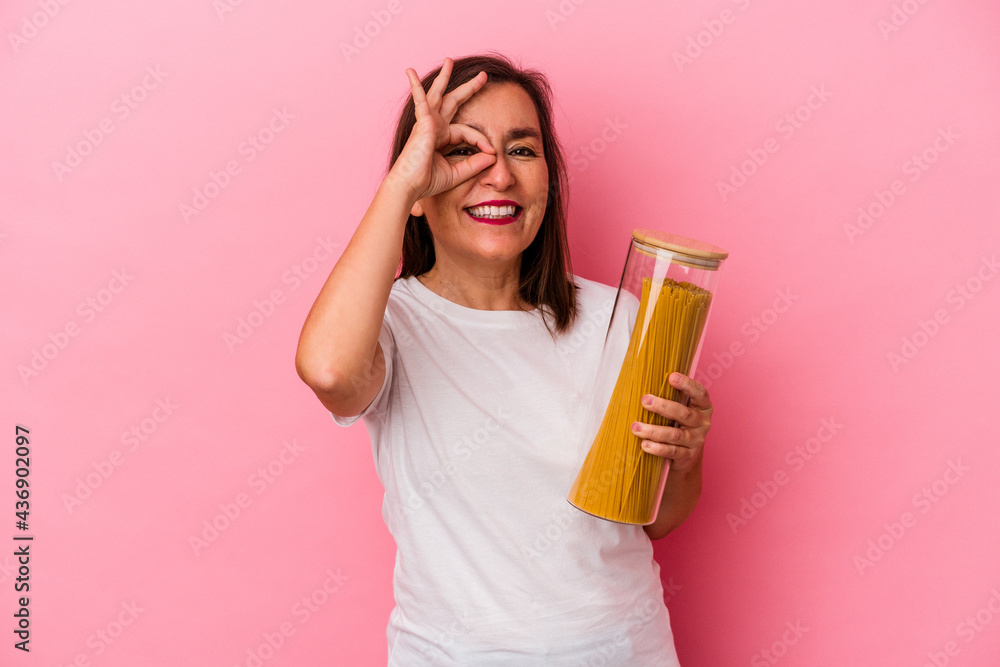 Middle age caucasian woman holding a pasta jar isolated on pink background excited keeping ok gesture on eye. Middle age caucasian woman holding a pasta jar isolated on pink background excited keeping ok gesture on eye.