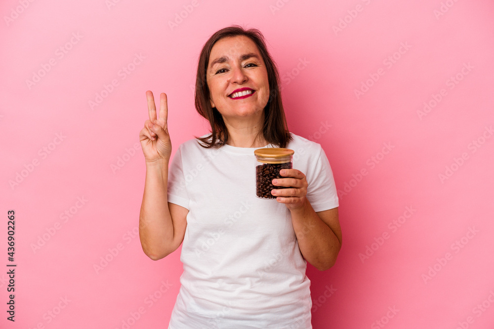 Middle age caucasian woman holding a coffee jar isolated on pink background showing number two with fingers. Middle age caucasian woman holding a coffee jar isolated on pink background showing number two with fingers.