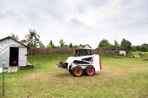 A skid steer loader clears the site for construction. Land work by the territory improvement. Machine for work in confined areas. Small tractor with a bucket for moving soil and bulk materials.