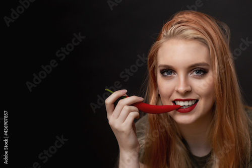 Portrait of smiling attractive  long hair young woman tasting chili pepper. There is enough space for your text in the photo.