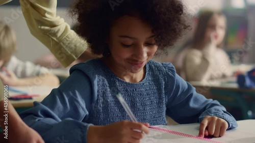 Girl talking with teacher in classroom. Smiling schoolgirl writing in notebook photo