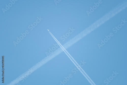 Low angle shot of intersecting plane trails in the blue sky forming an 