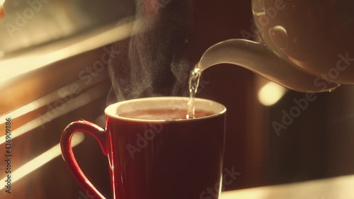 The teapot pours hot tea into a cup in the golden rays of the sun
