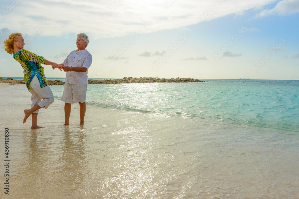 Romantic older couple walking, dancing, holding hands at the beach, by the seashore