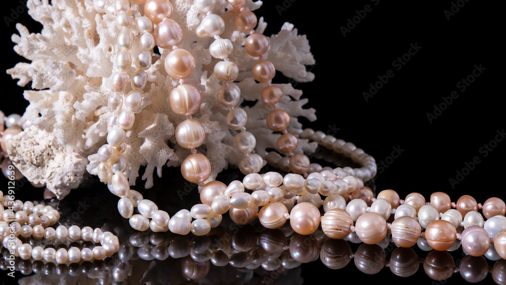 Iridescent pearl necklaces on a white coral. Isolated luxurious pearl jewelry on a black background close up with reflection. Iridescent pearl necklaces on a white coral. Isolated luxurious pearl jewelry on a black background close up with reflection.