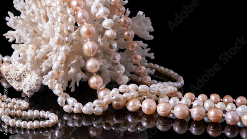 Iridescent pearl necklaces on a white coral. Isolated luxurious pearl jewelry on a black background close up with reflection. 