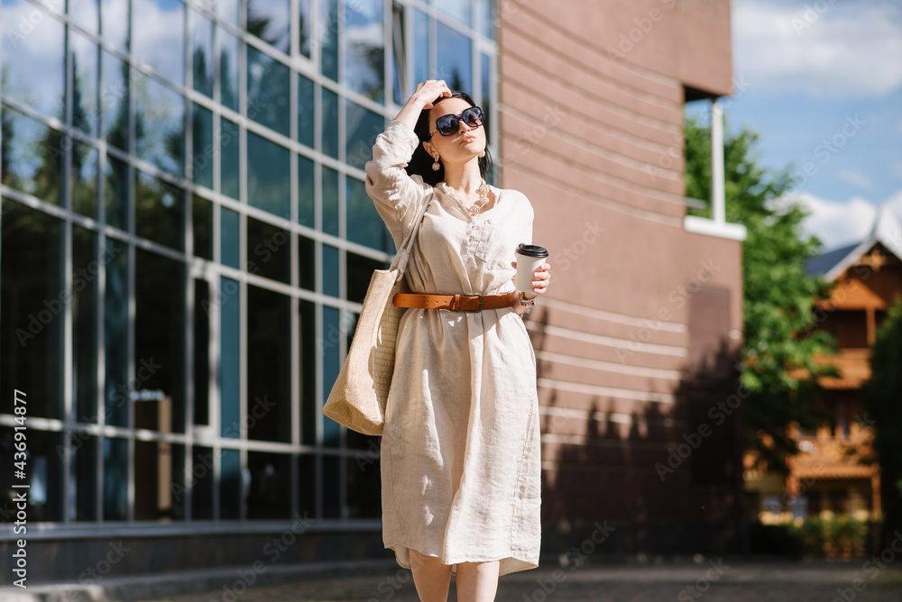 Brunette young woman with sunglasses and bag holding coffee walking in the city. Lifestyle portrait of woman Brunette young woman with sunglasses and bag holding coffee walking in the city. Lifestyle portrait of woman