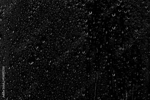 Drops of water flow down the surface of the clear glass on a black background. Texture for creativity. 