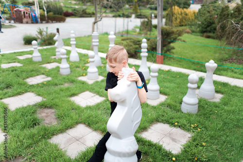 the boy on the lawn with the huge chess pieces picked up the horse and moved it one move further