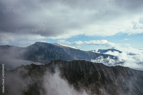 Wonderful foggy scenery with great rocks and mountains in low clouds. Atmospheric misty landscape with mountain wall and glacier in clouds. Beautiful view to rocky wall and snow mountains in clouds.