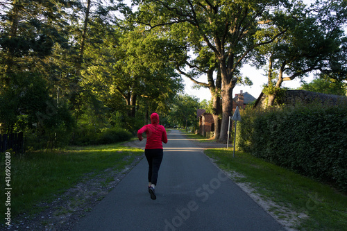 A young woman jogging in the street of a green park at sunset