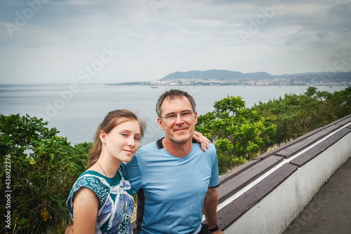 Portrait of travelers. A man and a teenage girl are sitting on vacation, hiking. The man is happy and smiling during the hike. Father and daughter in the foreground, they have a beautiful view © Ekaterina Utorova