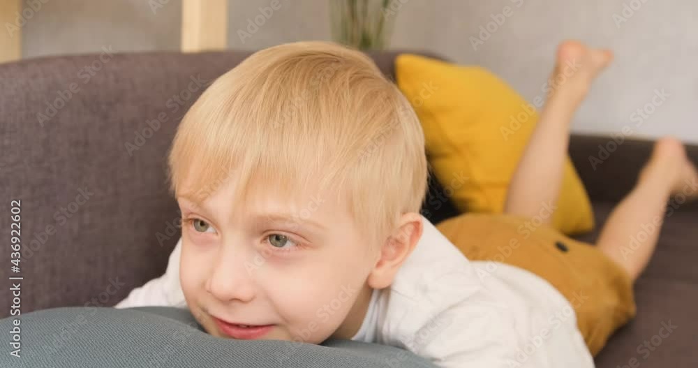 Little happy blond boy lies on the couch and waves his legs. Daylight Little happy blond boy lies on the couch and waves his legs. Daylight