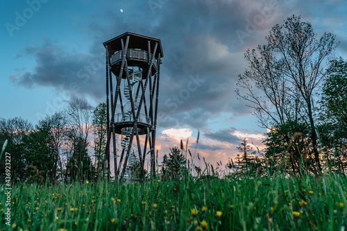 Lookout tower called Na Vetrne Horce at sunset, Broumov region,Czech Republic.Wooden tower with spiral staircase on blooming meadow fresh spring scenery.Travel explore concept.Modern architecture photo