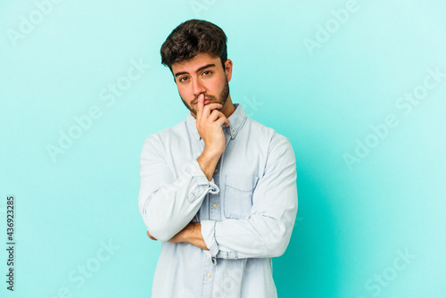 Young caucasian man isolated on blue background unhappy looking in camera with sarcastic expression. © Asier