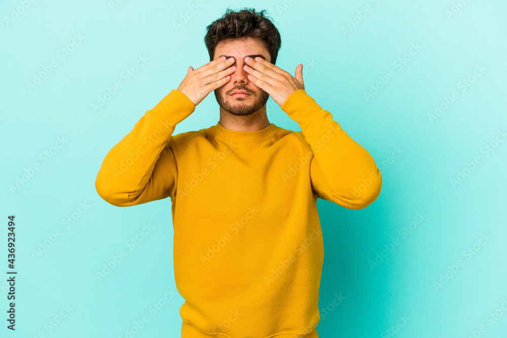 Young caucasian man isolated on blue background afraid covering eyes with hands. Young caucasian man isolated on blue background afraid covering eyes with hands.