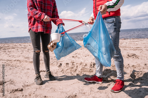 cropped view of couple with trash bags and grabbers picking up garbage on sand