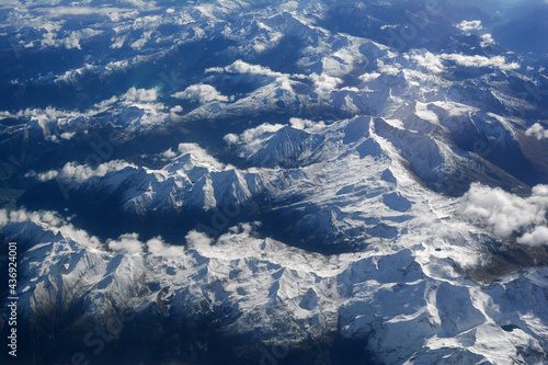 Aerial view of snowy mountains and clouds, opposite the sunlight