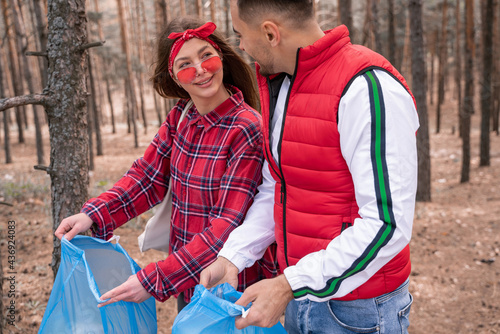 happy couple with trash bags looking at each other in forest