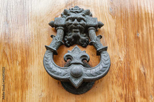 Old metal knocker with satyrs head on a wooden door, Florence, Italy