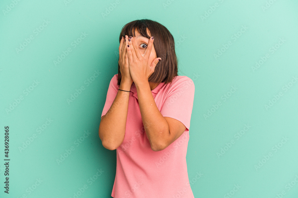 Young mixed race woman isolated on blue background blink through fingers frightened and nervous. Young mixed race woman isolated on blue background blink through fingers frightened and nervous.