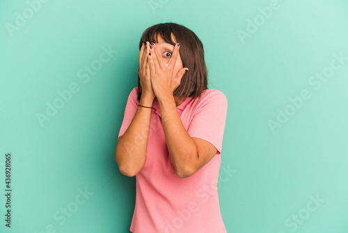 Young mixed race woman isolated on blue background blink through fingers frightened and nervous. © Asier