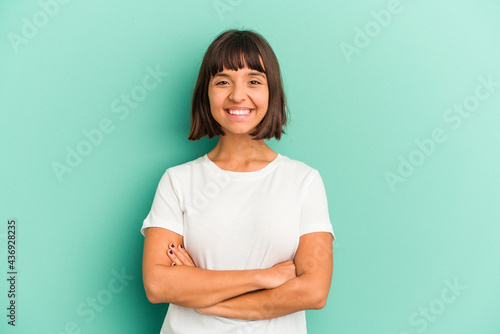 Young mixed race woman isolated on blue background who feels confident, crossing arms with determination.