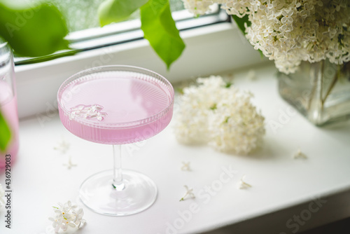 Fresh pink non alcoholic cocktail in glass with lilac flowers against window background.