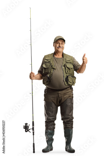 Full length portrait of a fisherman in a uniform standing with a fishing rod and showing thumbs up