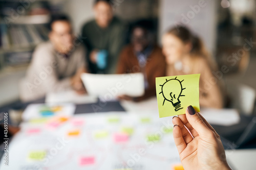Close-up of creative woman holding paper with light bulb during business meeting in the office.